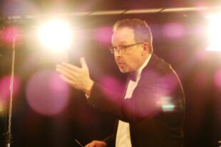 2023-3-27-BI-bia-Blasorchester-und-Dirigent inmitten von Lichtreflexen